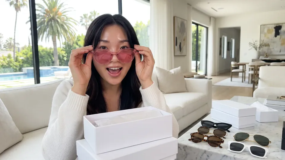 A creator trying on tinted sunglasses on camera, product boxes in front of her.